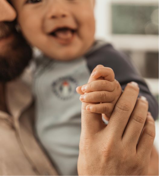 Baby hält mit Hand Zeigefinger eines Mannes fest.